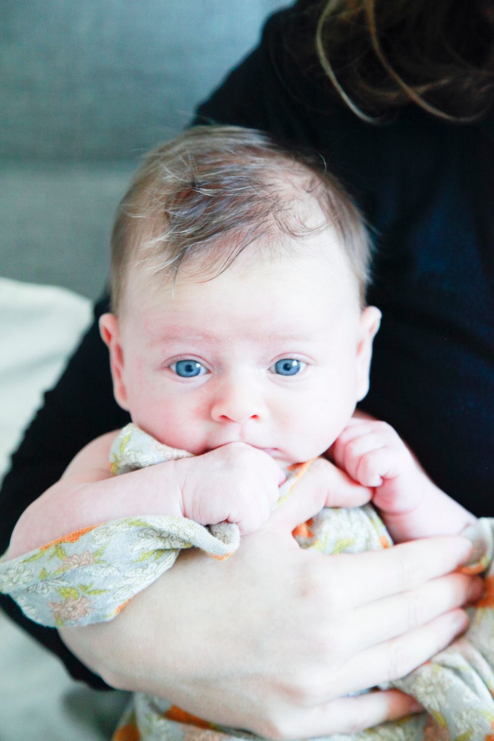 Close-up series of a baby with bright blue eyes being cradled against dark background.