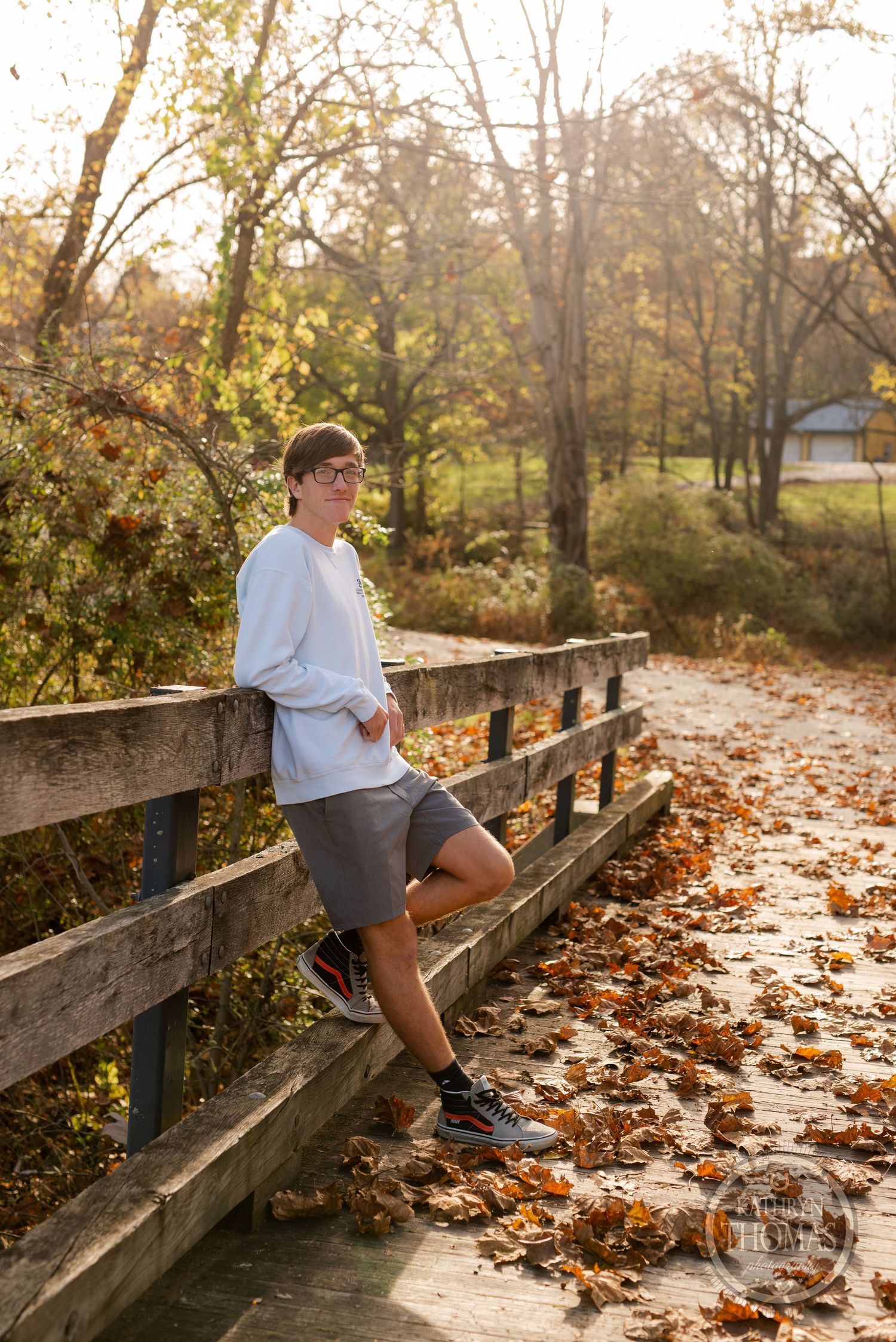 Athletic person in casual wear stands on wooden bridge with fallen autumn leaves.