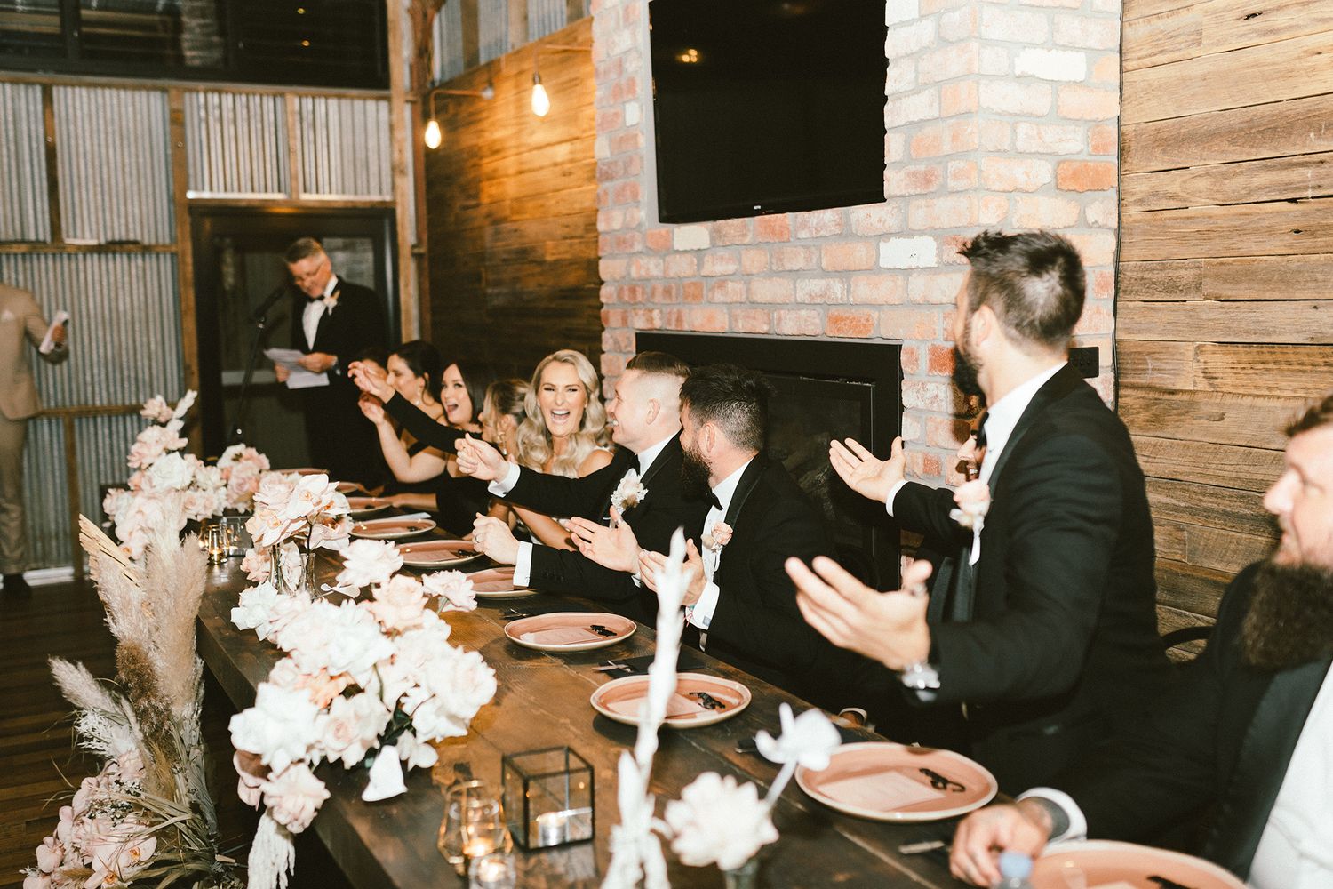 Wedding reception dinner with guests seated at long table decorated with white floral centerpieces.