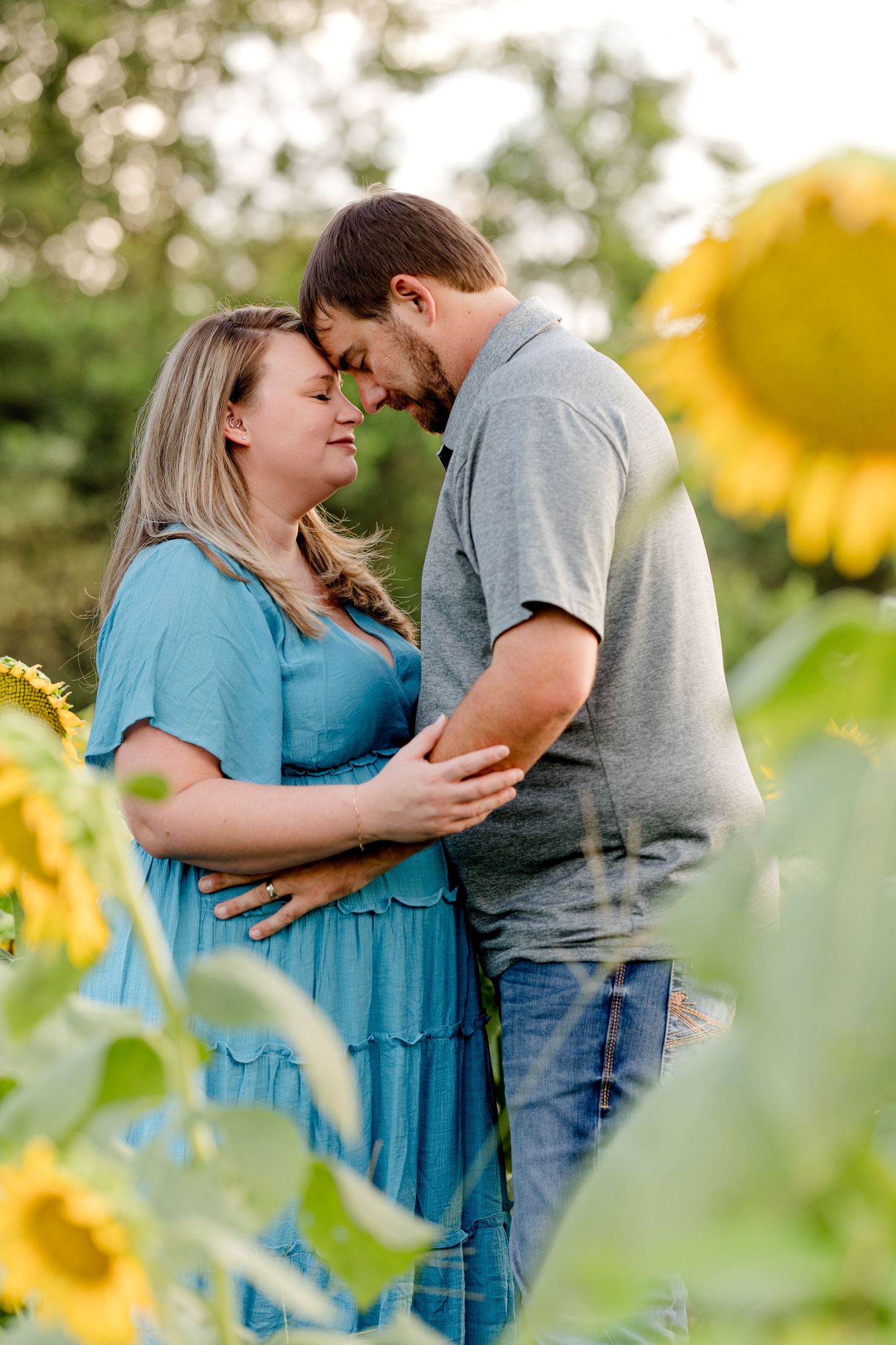 Romantic couple embracing in sunflower field during maternity photo session.