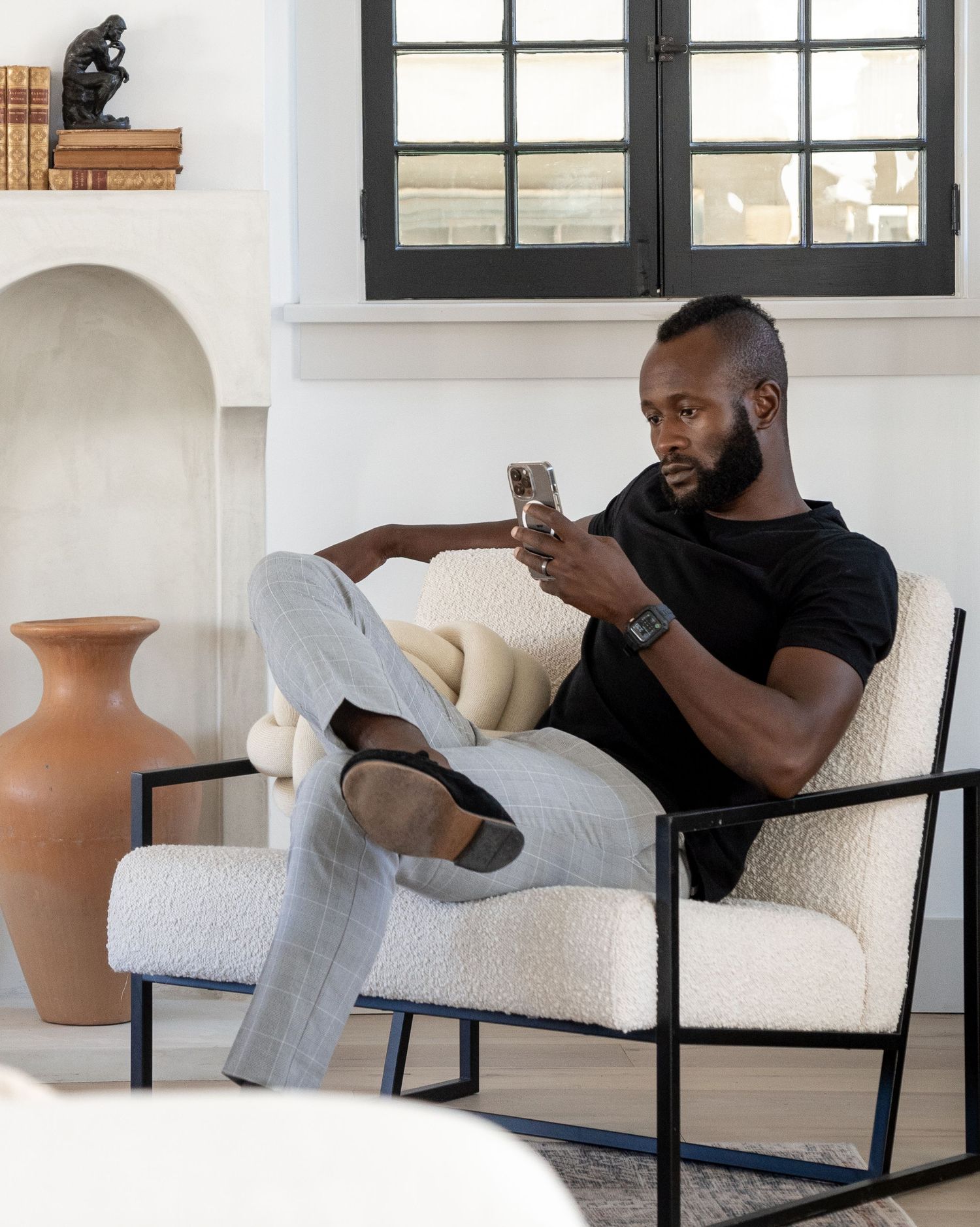 A person relaxes in a modern white armchair while checking their phone in a minimalist interior setting.