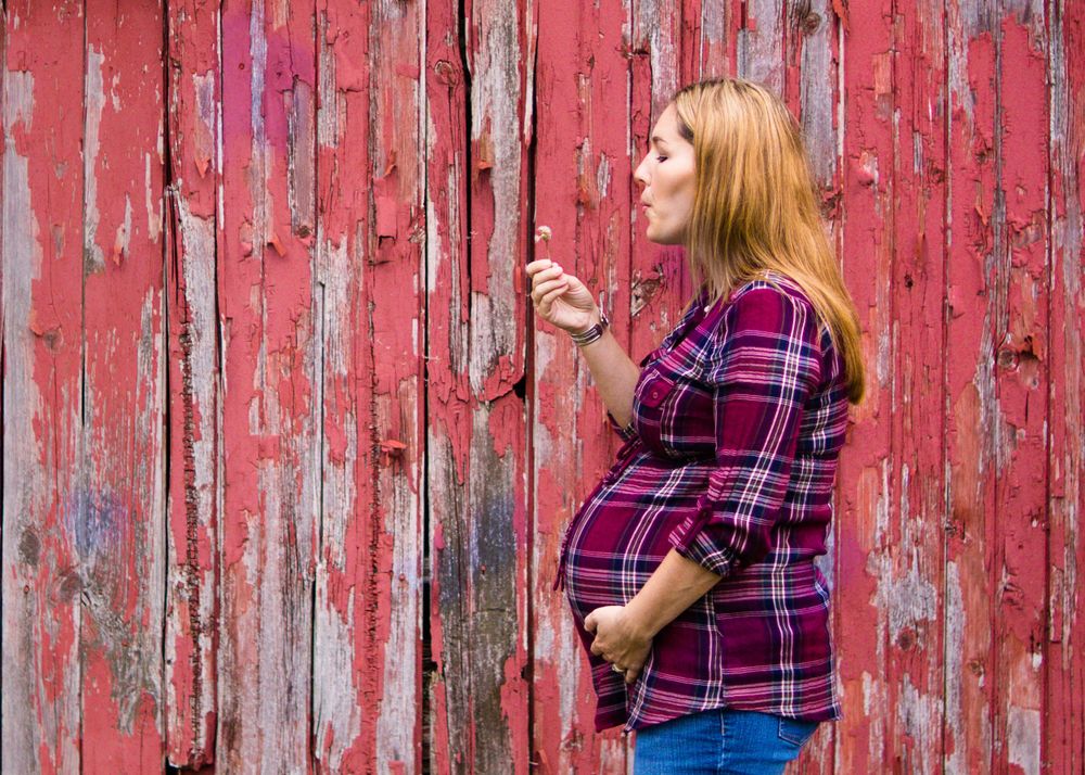 Outdoor photo of pregnant woman blowing bubbles by a barn during a maternity session by professional maternity photographer in Dandridge