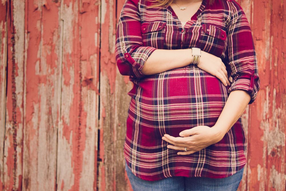 Photo of a woman holding her pregnant stomach standing in front of a barn for a maternity photo session.