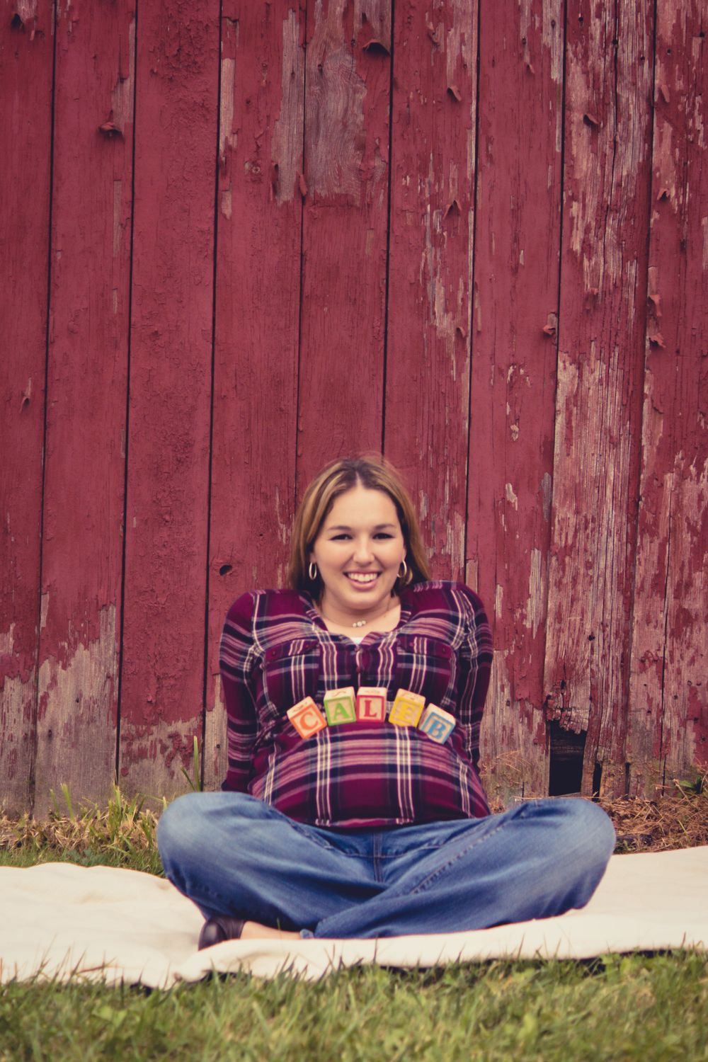 Photo of a pregnant woman sitting in front of a barn with blocks spelling her baby's name perched on her belly