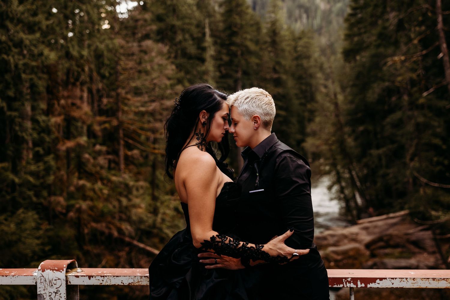 Romantic couple embracing on a bridge surrounded by evergreen forest.