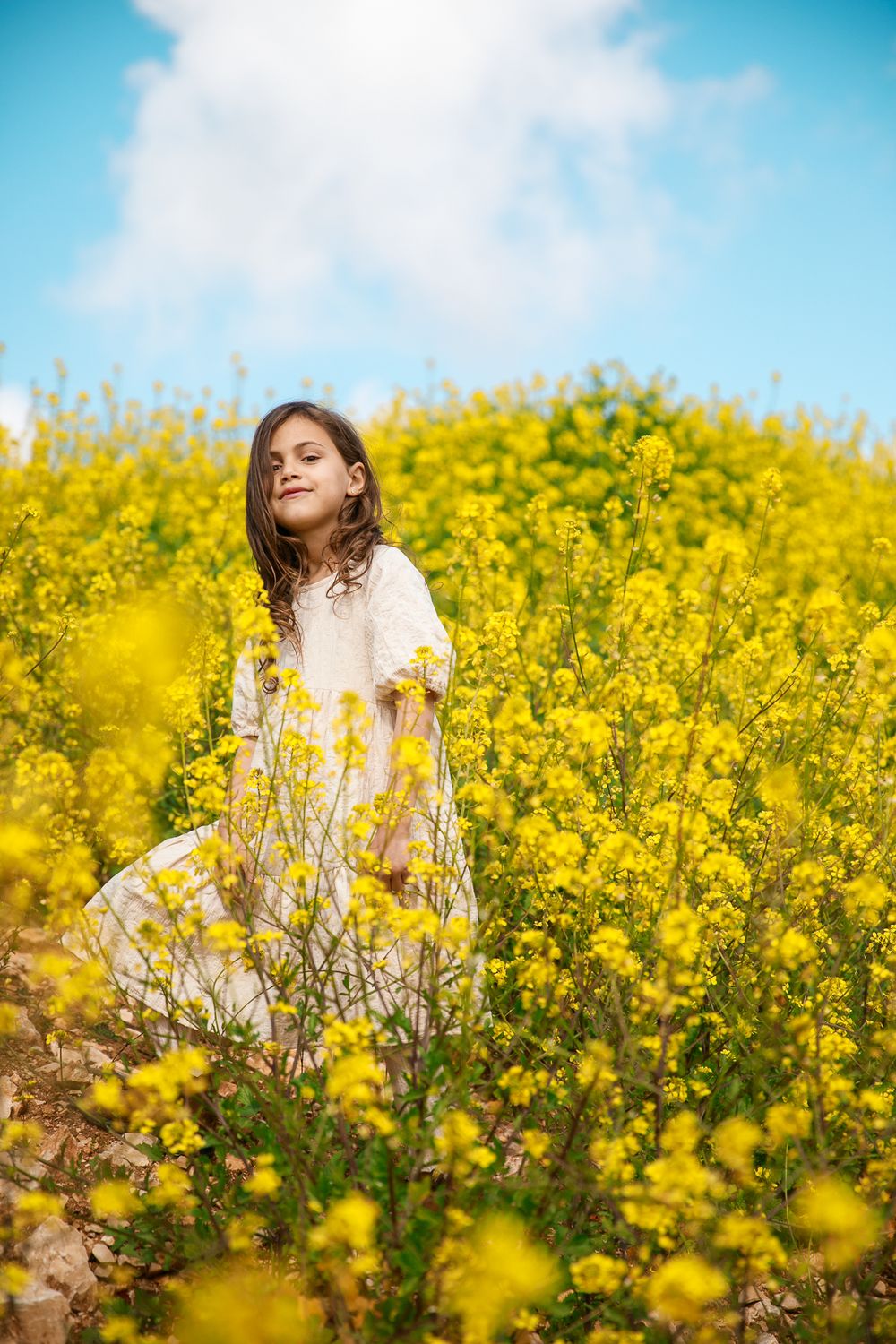 A girl smiles at the camera in a field of yellow flowers