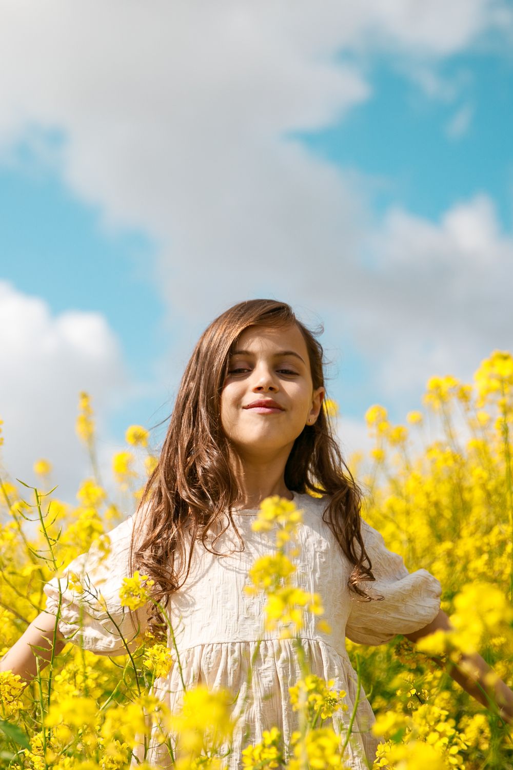 A girl smiles at the camera in a field of yellow flowers