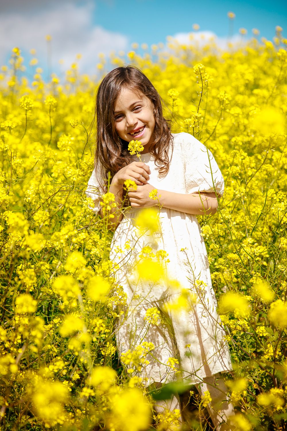 A girl smiles at the camera in a field of yellow flowers