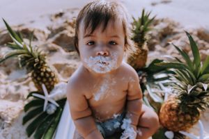 Baby with messy face from cake smash surrounded by tropical pineapples.