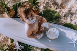 Overhead view of baby covered in cake frosting with pineapples on beach.