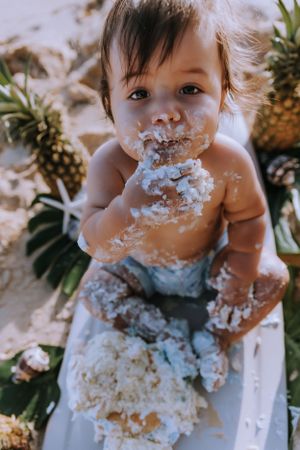 Baby covered in white frosting during beach cake smash with pineapples.