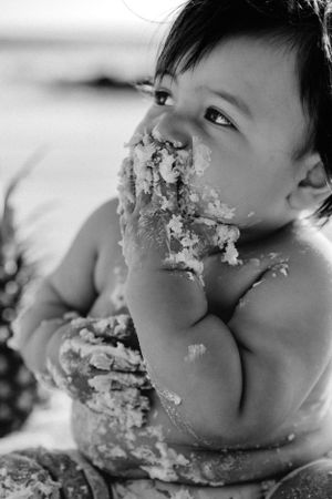 Black and white portrait of baby covered in cake during beach photoshoot.