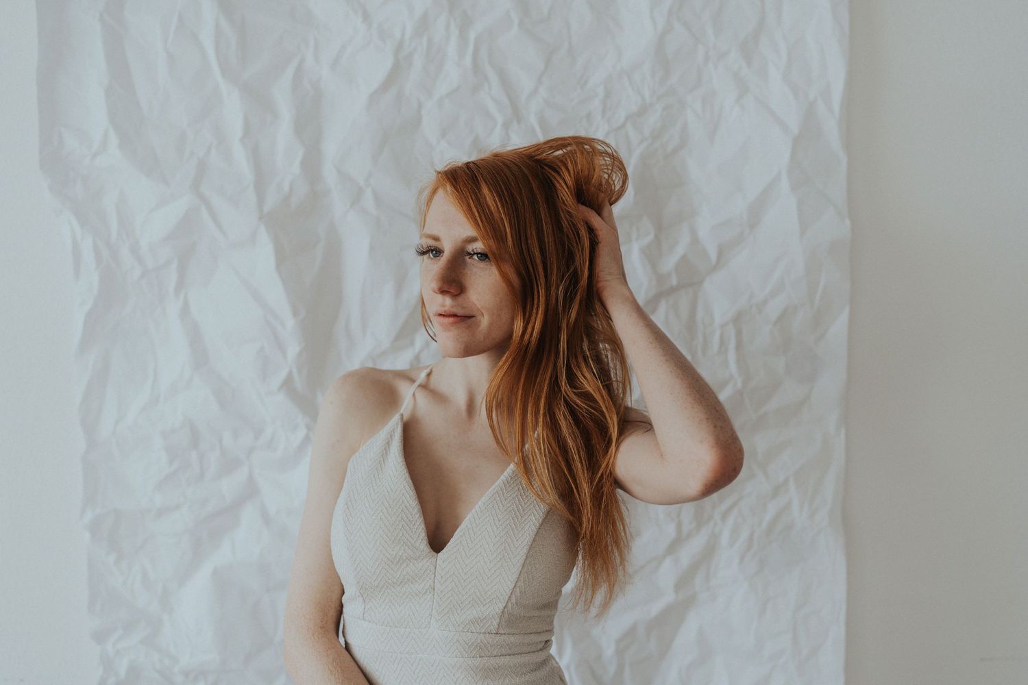 A redhead woman stands against a white wall