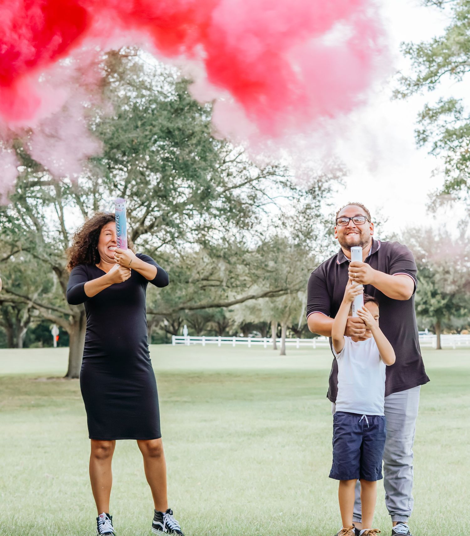 A couple celebrating with pink smoke bombs in an outdoor park setting.