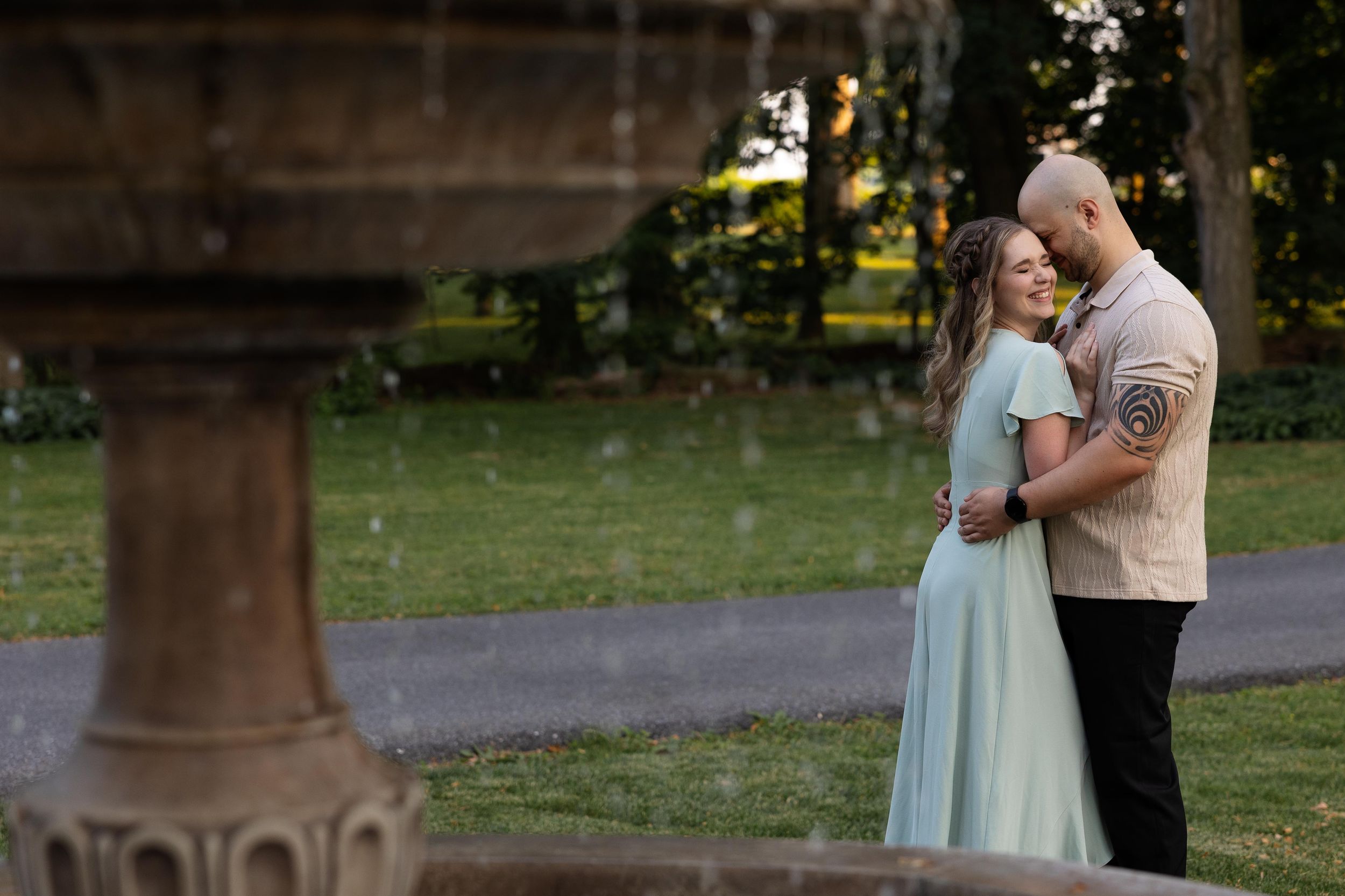 A couple shares a gentle embrace near a decorative stone fountain at dusk.