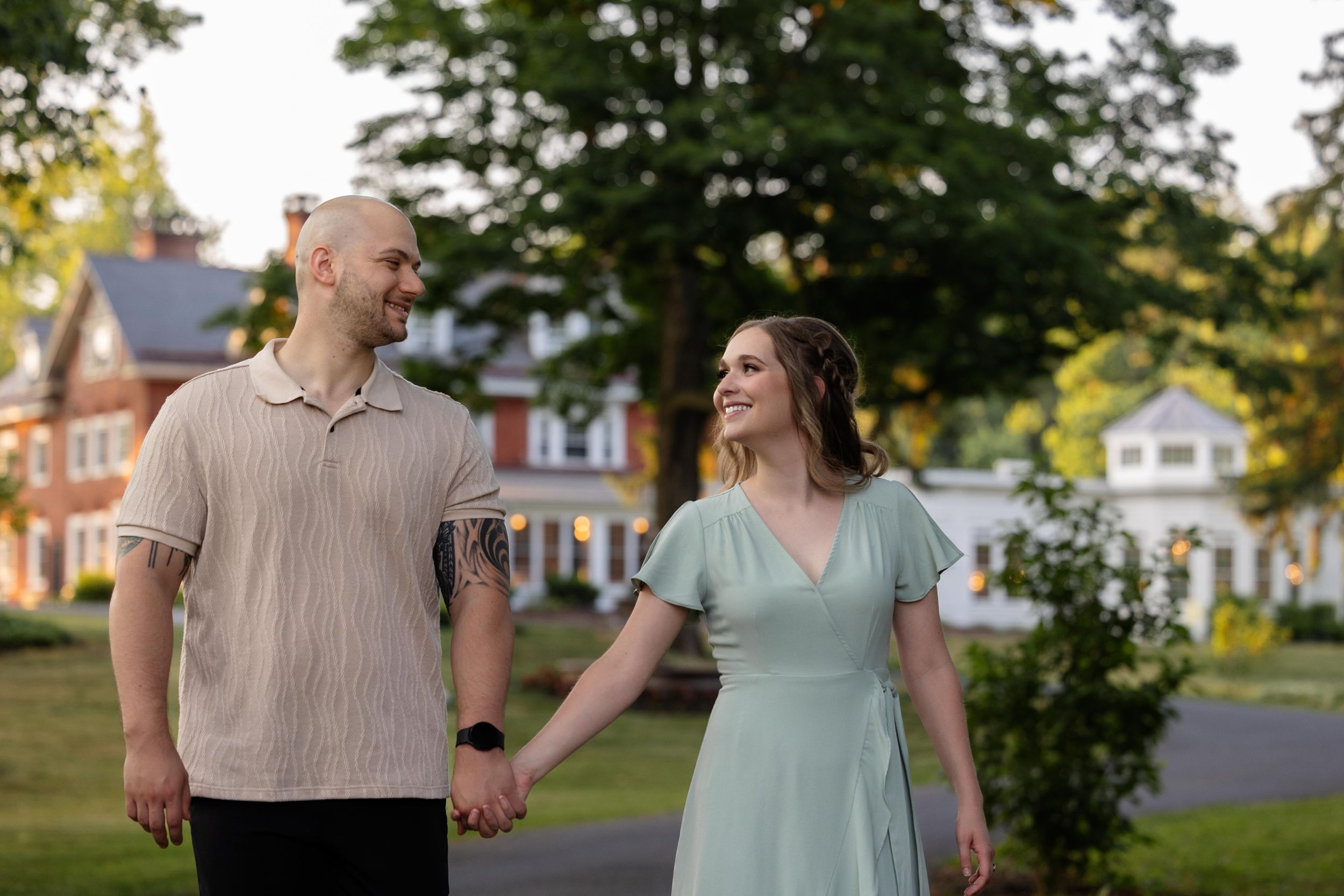 A couple walking hand in hand on a residential street with historic homes in the background.
