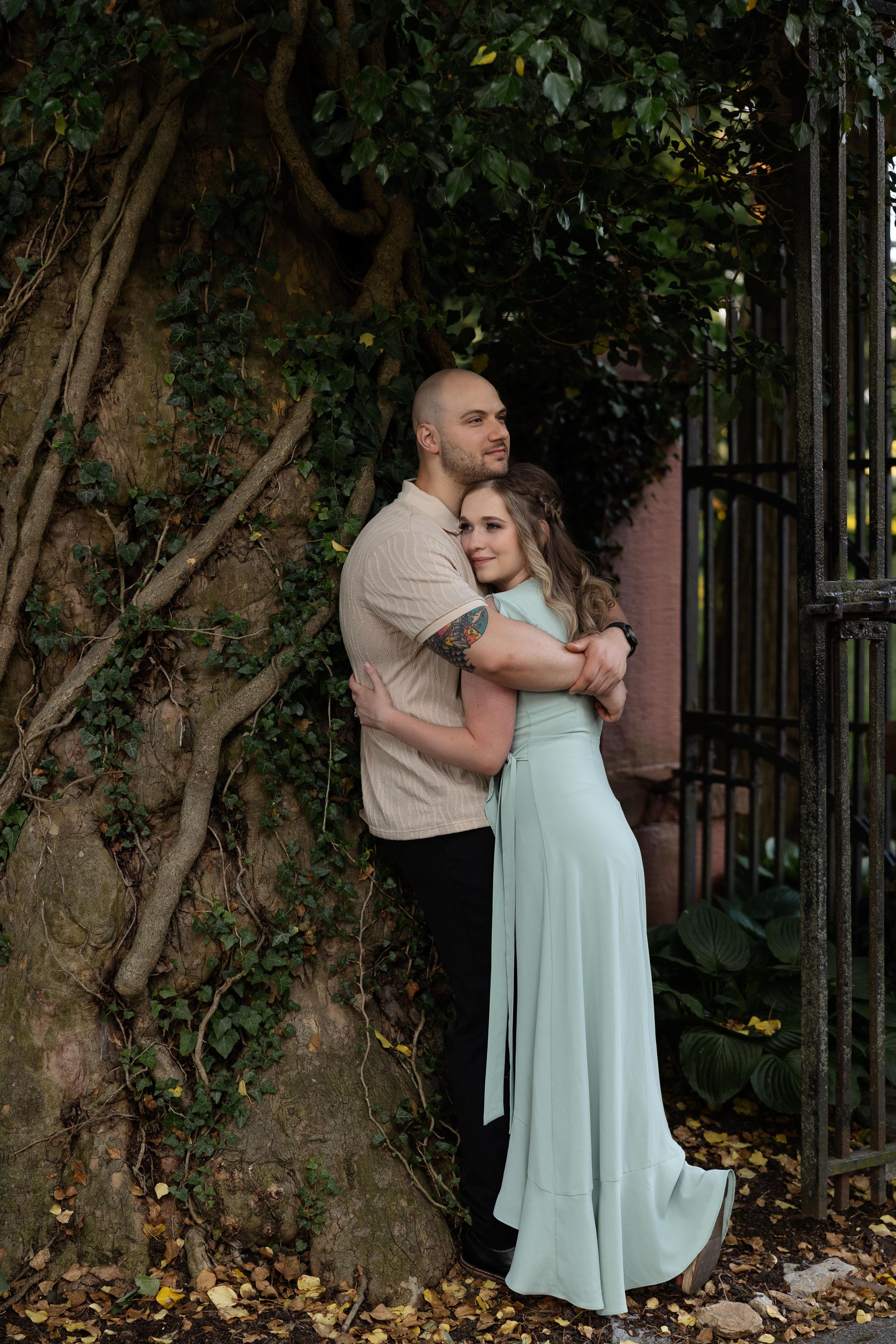 Couple embracing against a vine-covered wall next to a wrought iron gate in romantic lighting.