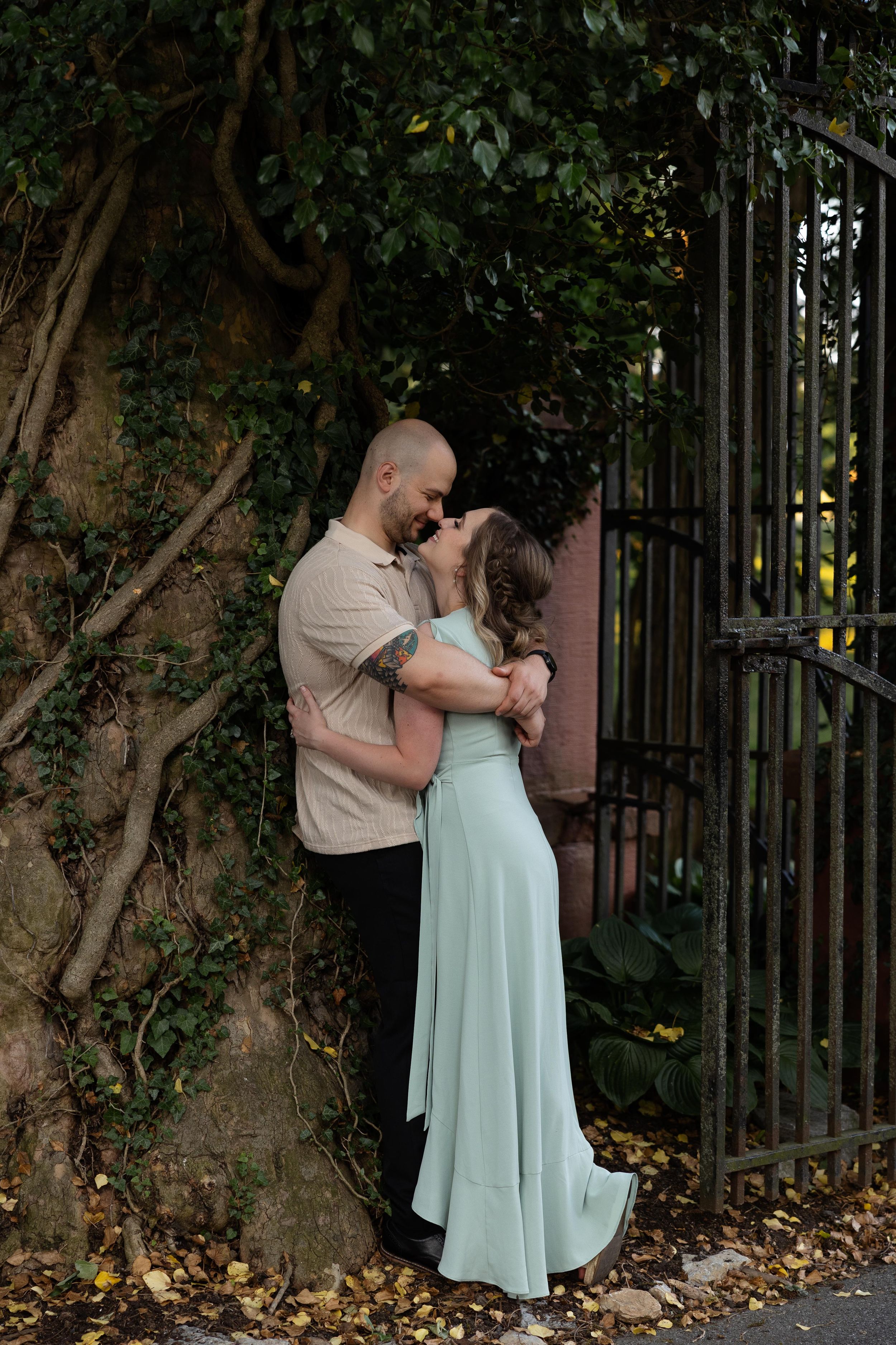 Intimate portrait of a couple embracing against a textured wall with climbing vines.