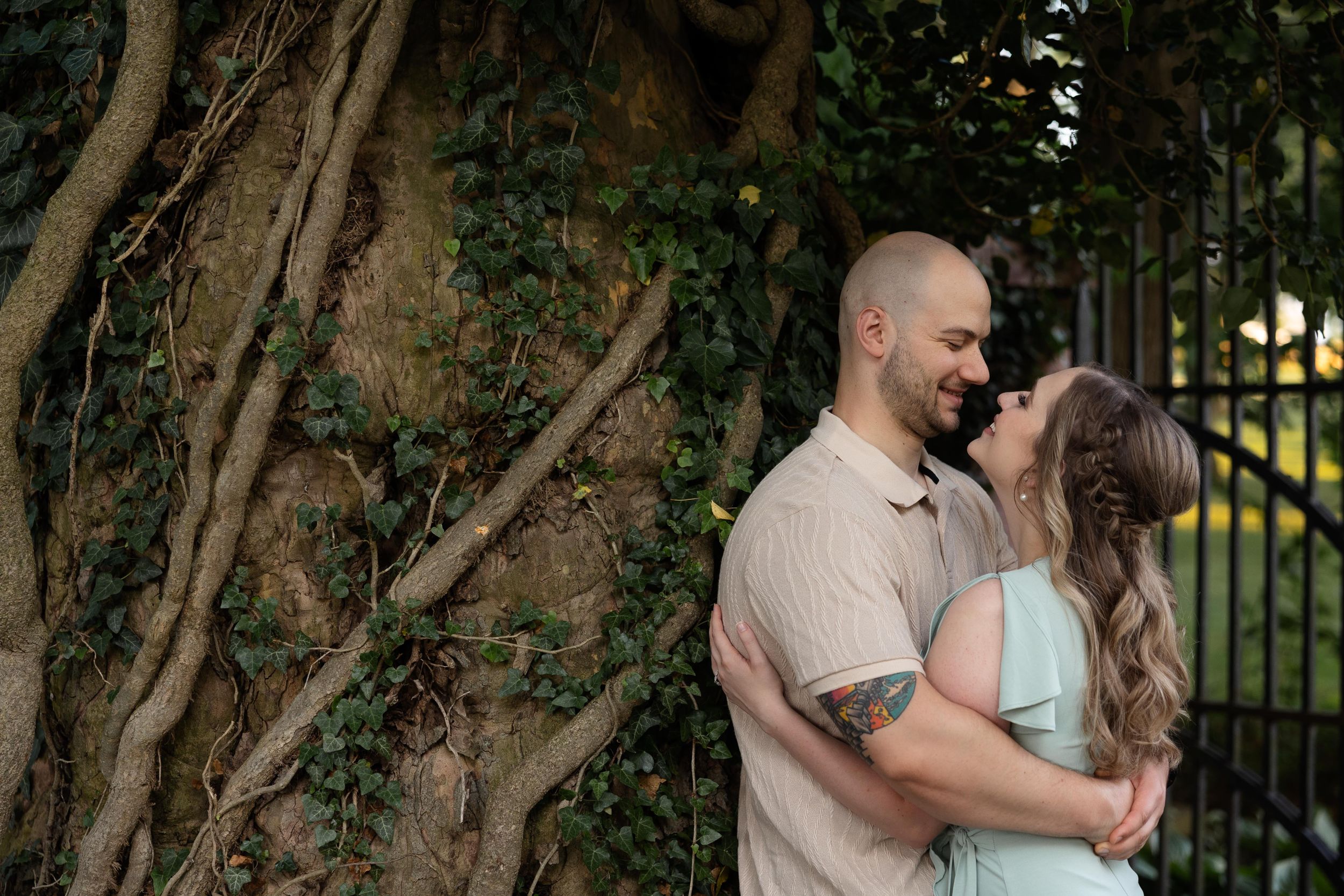 Tender moment between a couple standing against a tree-covered wall during a photo session.