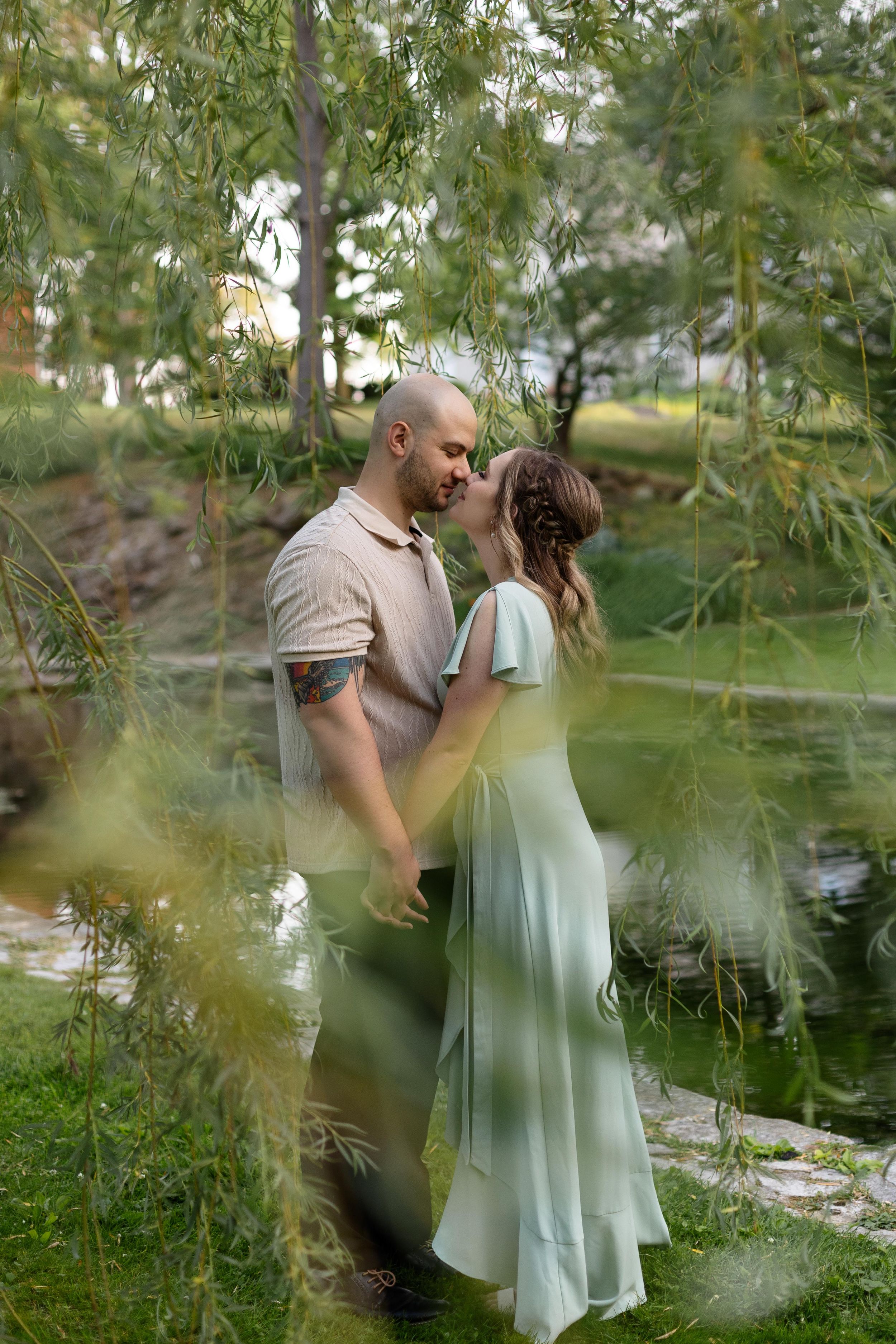 Romantic portrait through willow tree branches near a pond.