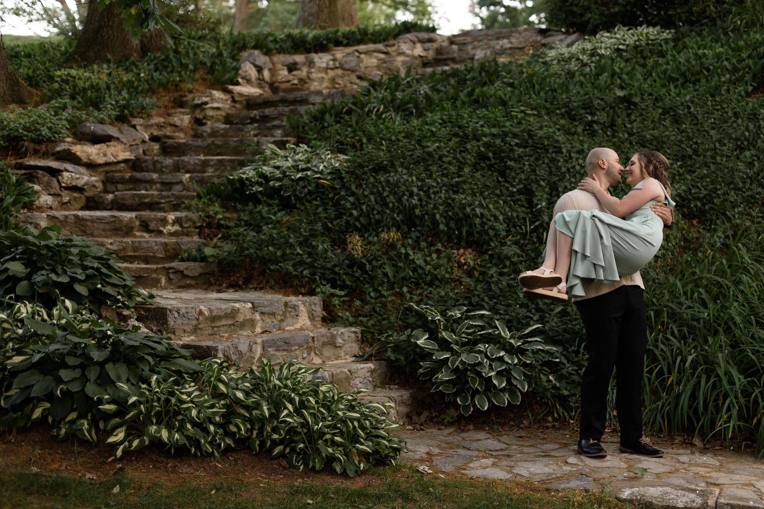 A couple shares an intimate moment on stone steps surrounded by lush garden landscaping.