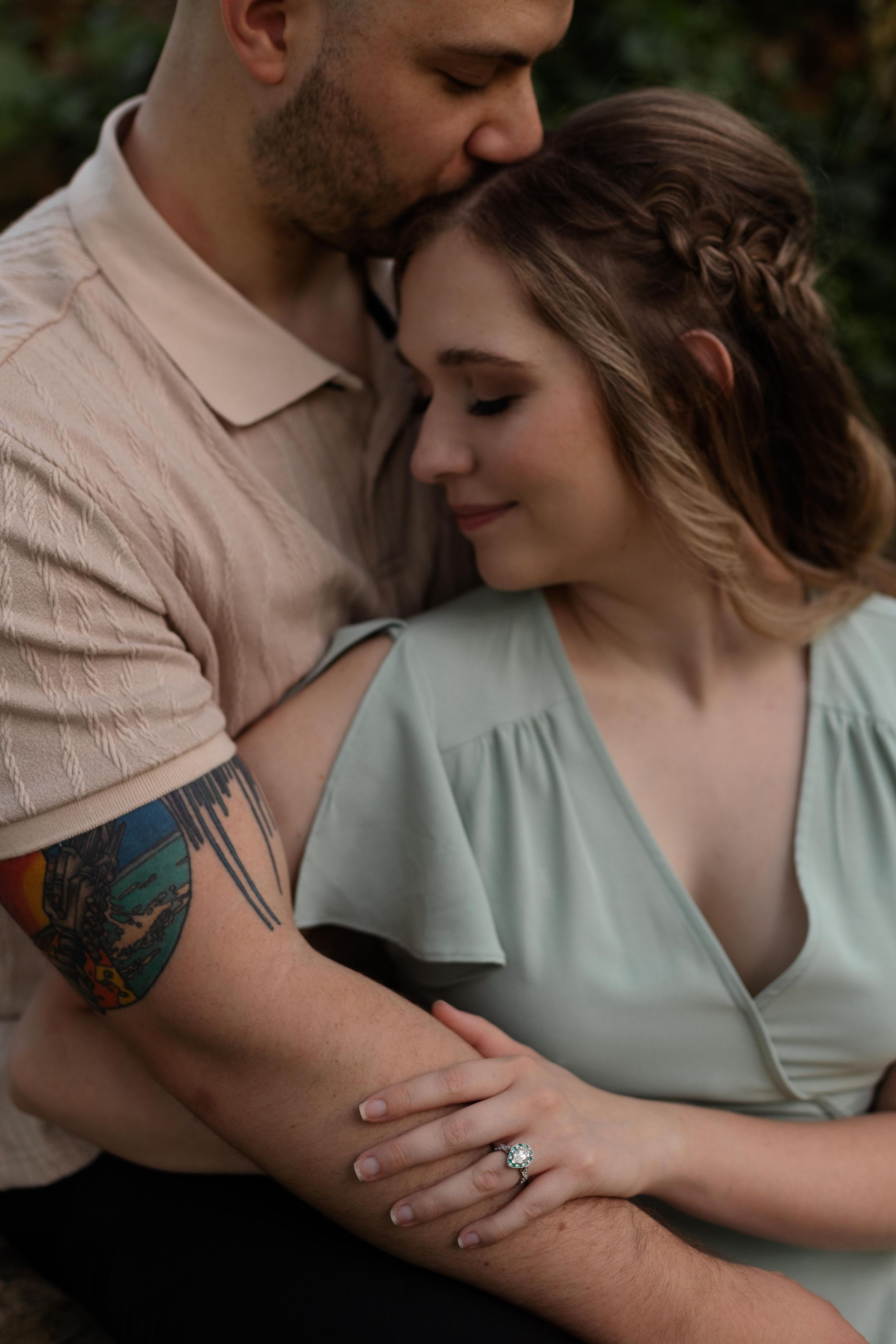 A tender embrace captured in soft light showing detailed tattoo art and a mint green dress.