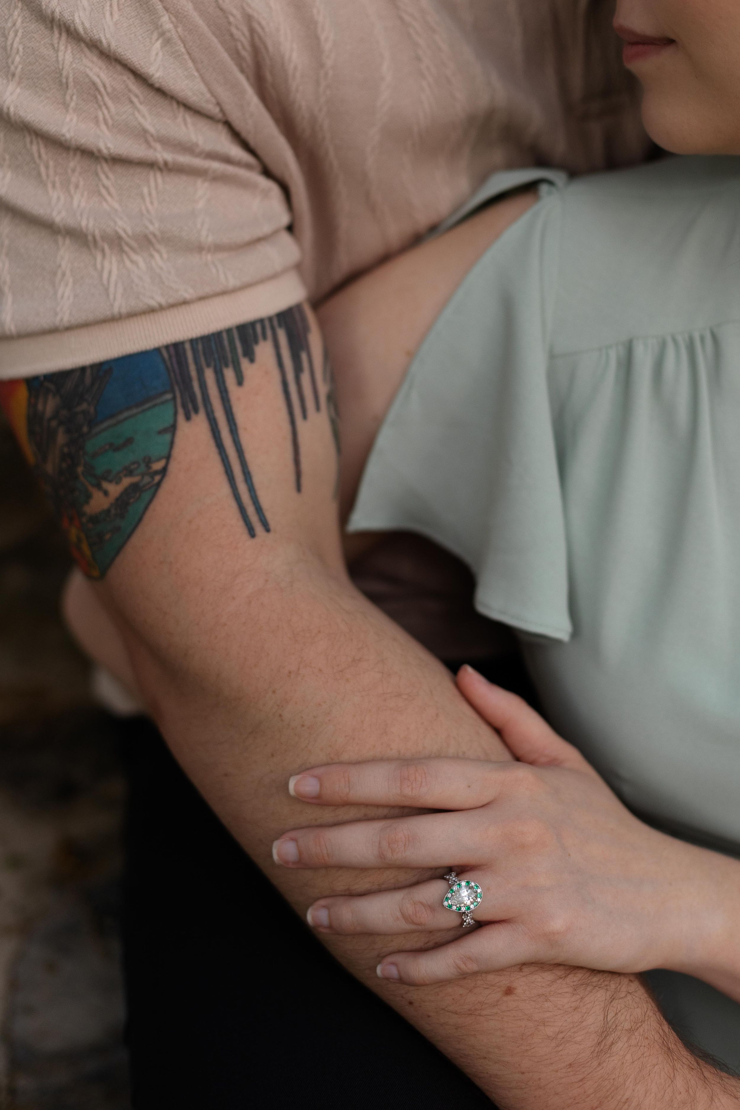 Close-up detail of colorful arm tattoo and engagement ring as couple embraces.