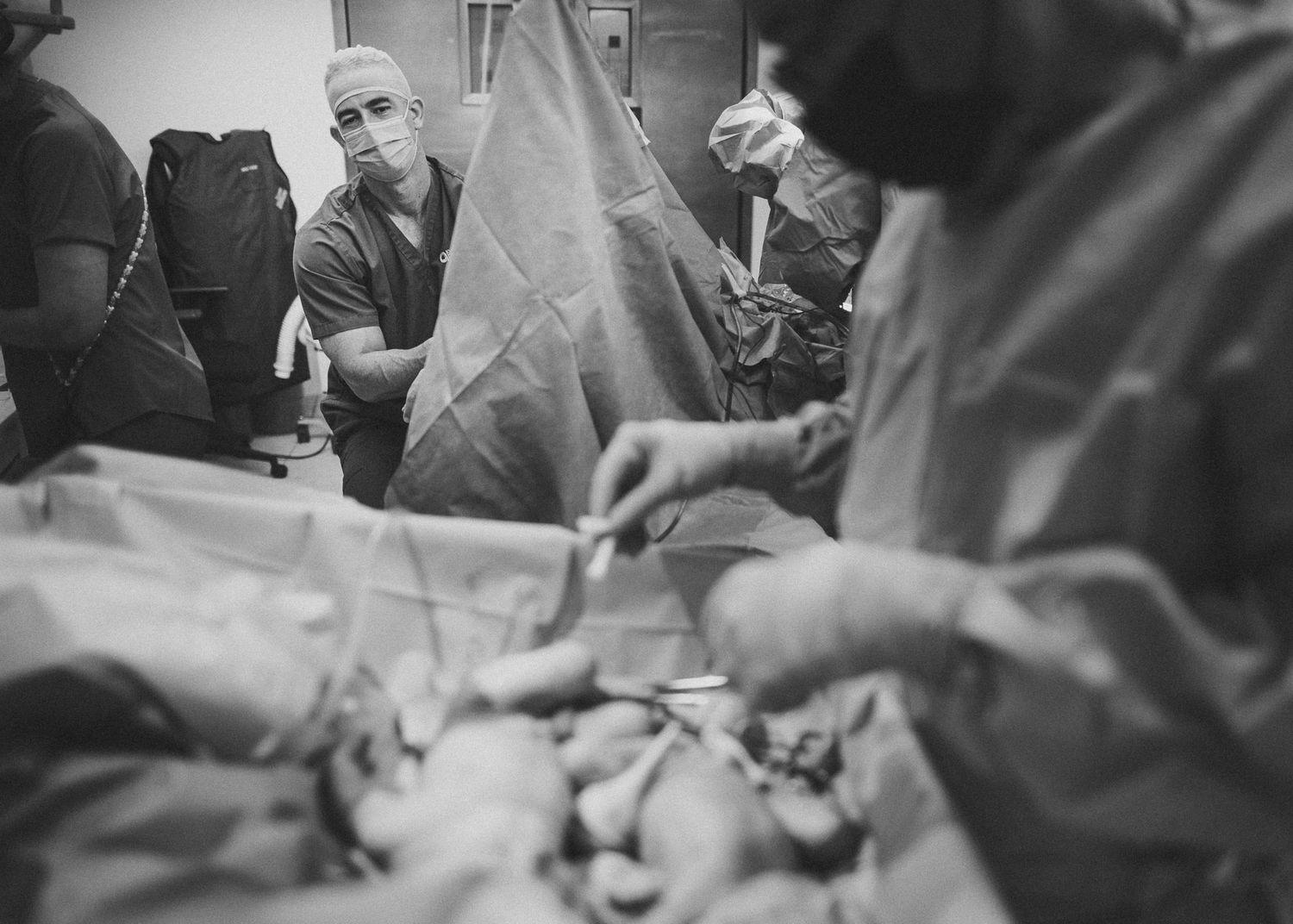 Surgical team performing operation with medical instruments and drapes visible.