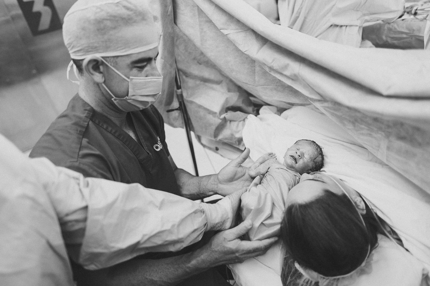 Medical professional in surgical mask examines newborn infant in black and white historical photograph.
