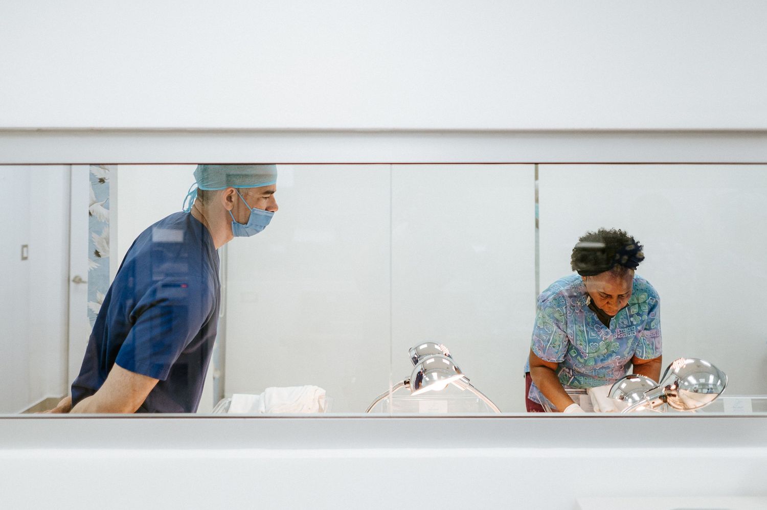Healthcare workers in scrubs attend to newborns through hospital nursery window.