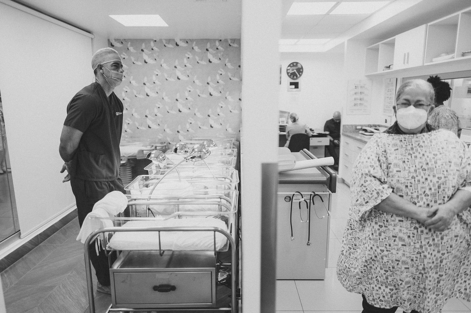 Medical personnel in protective gear working in hospital nursery with patient rooms.