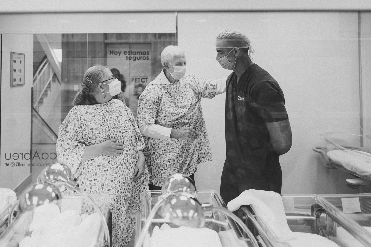 Healthcare workers discuss patient care in hospital maternity ward hallway.