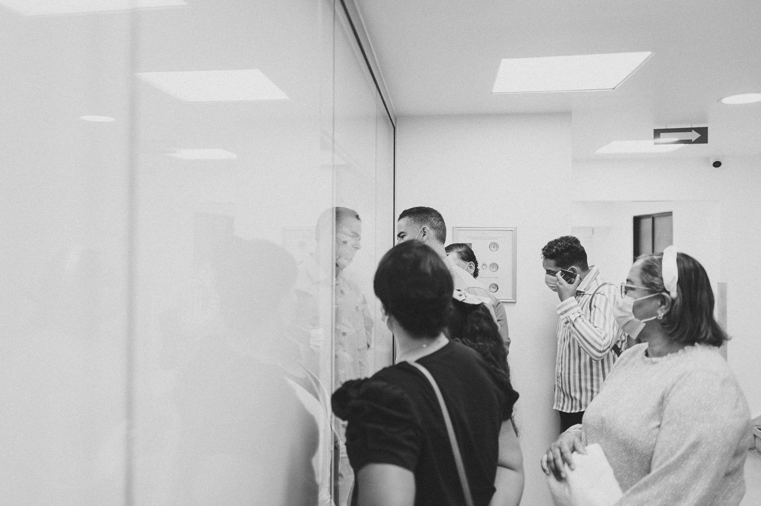People wearing masks gather in a clinical setting with white walls and fluorescent lighting.