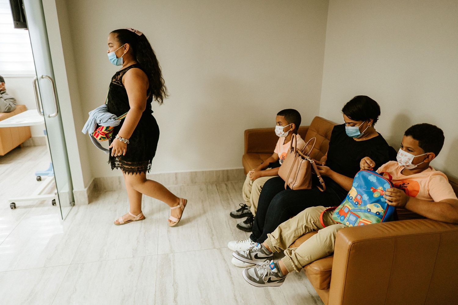 Family members sitting on a couch while someone walks past a window.