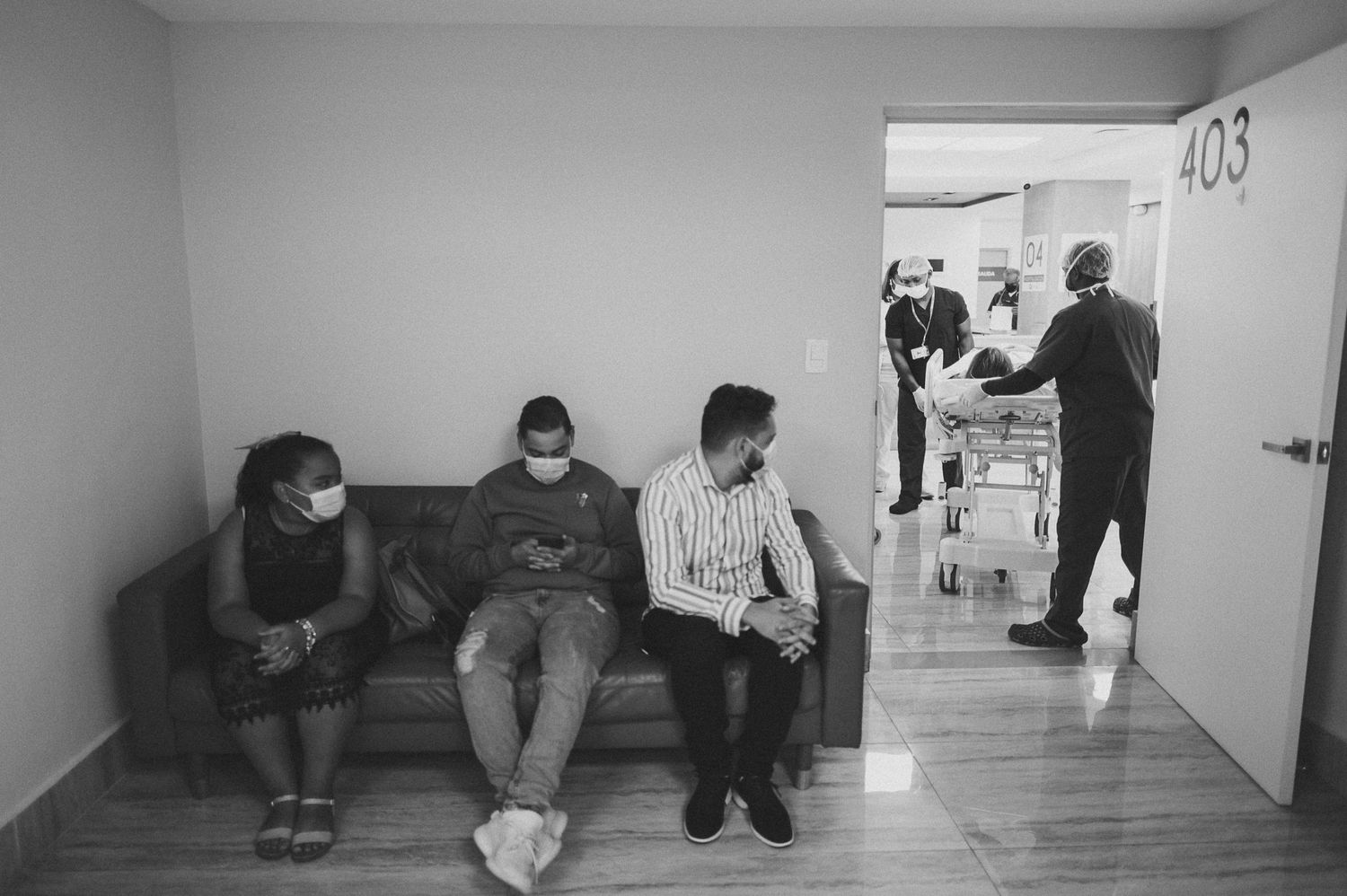People sitting on a couch in a hospital waiting area near a doorway.