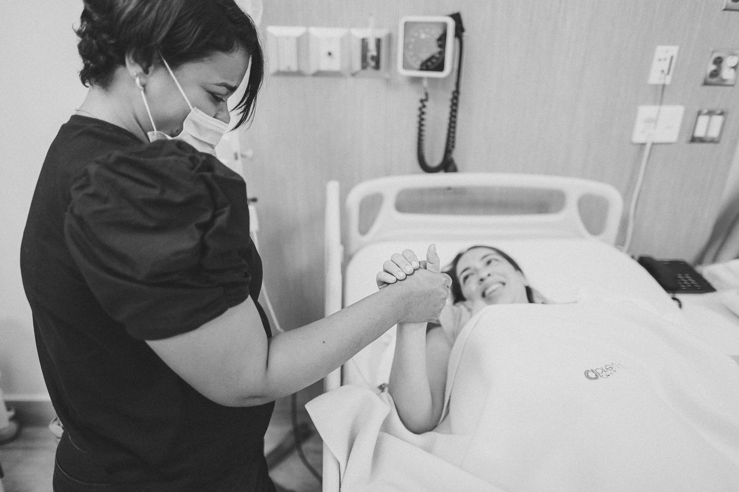 Healthcare worker in mask providing care to patient in hospital bed.