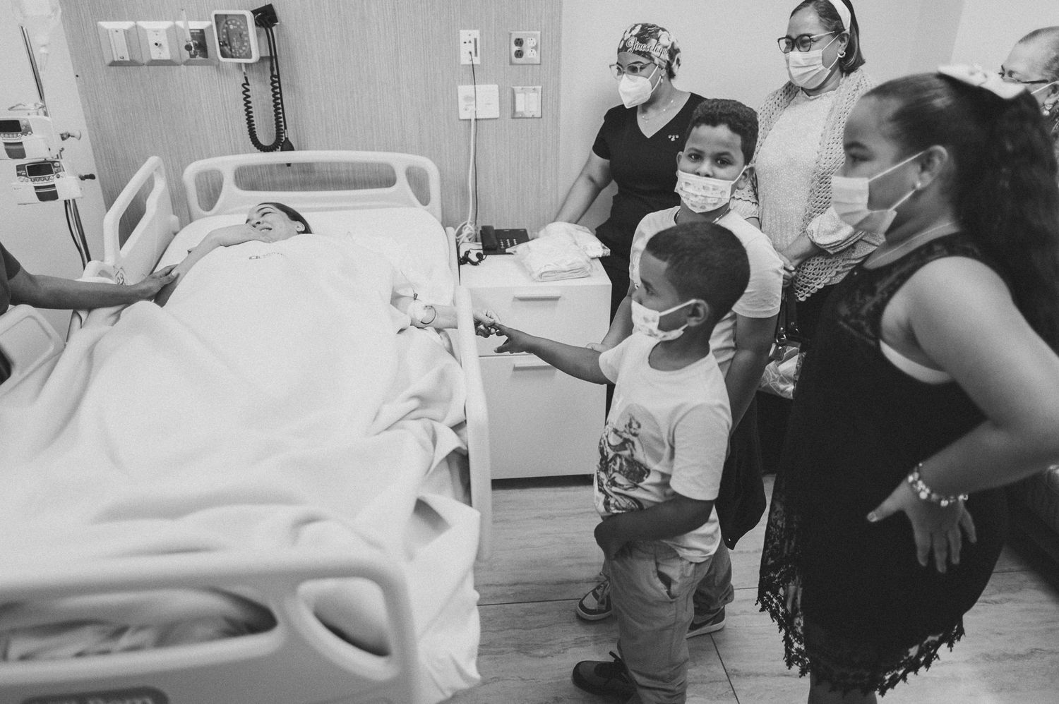Medical staff and visitors gathered around hospital bed during patient care.