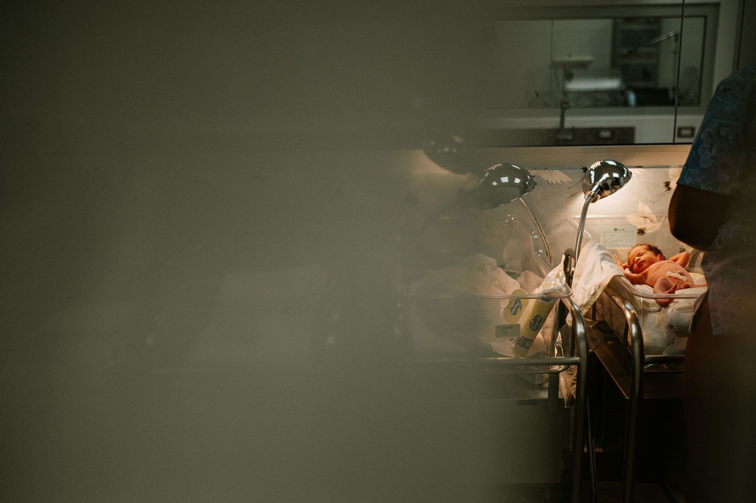 Dimly lit hospital room with medical equipment visible in background.