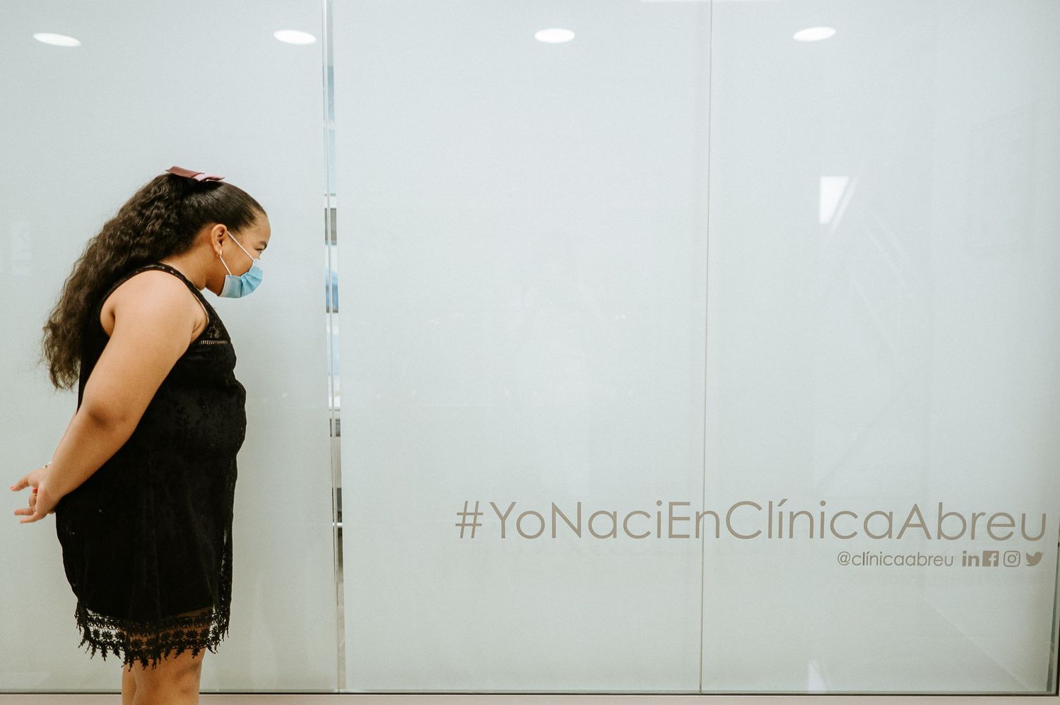 Woman standing against white wall with Spanish text overlay.