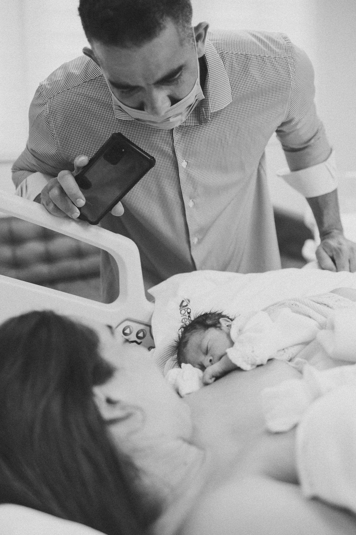 Black and white hospital photo of newborn with medical staff wearing protective mask.