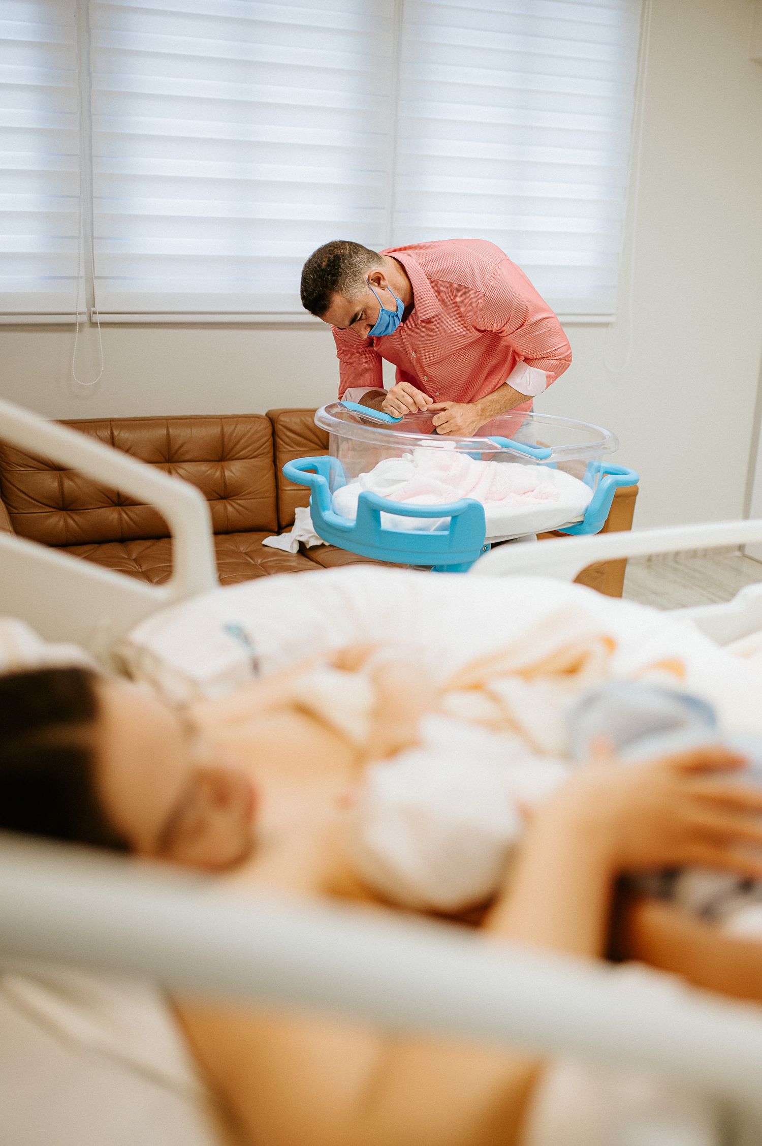 Medical professional in coral shirt filling out paperwork near hospital bed.