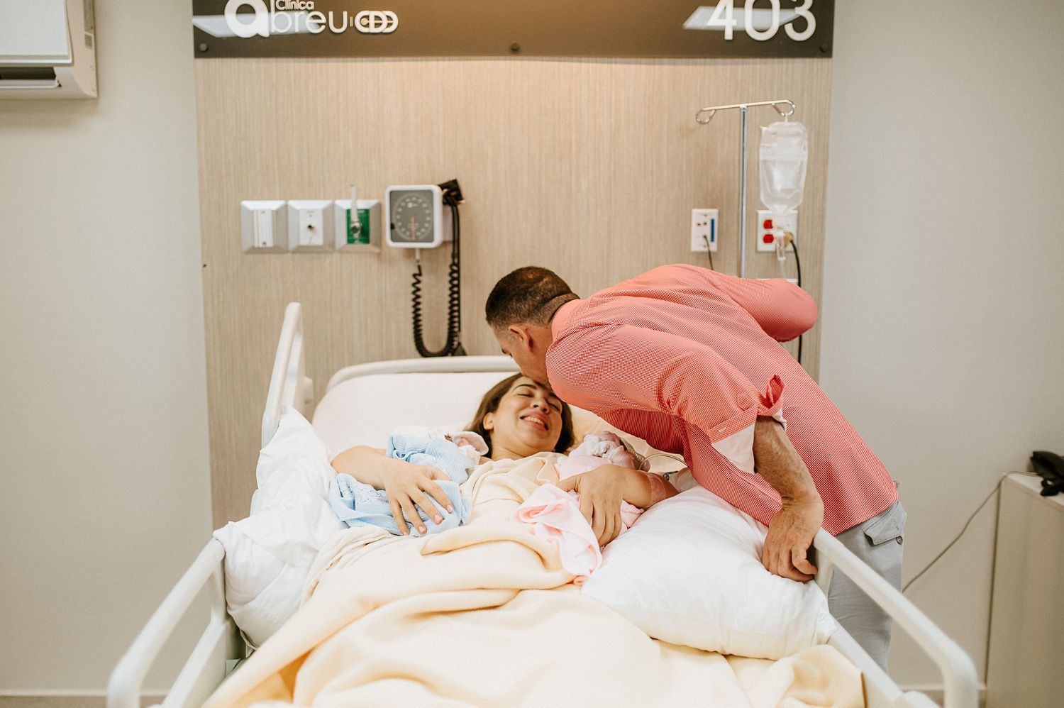 Healthcare provider wearing pink checks on patient and newborn in hospital room.