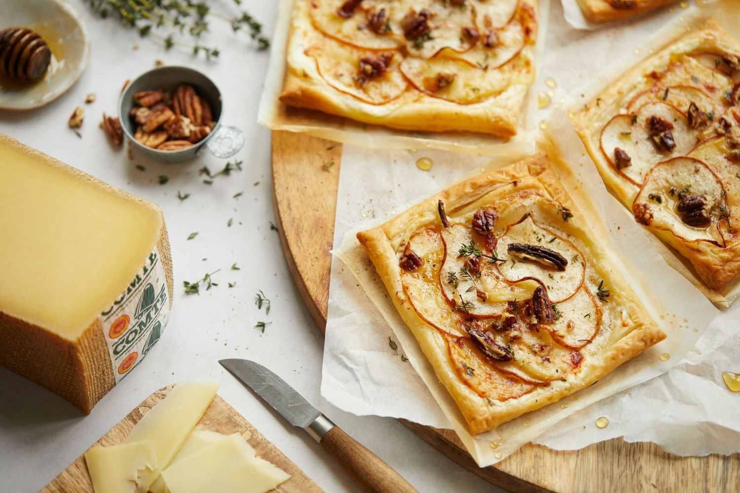 Savory pastries with cheese and nuts arranged on parchment paper with Comte cheese block.