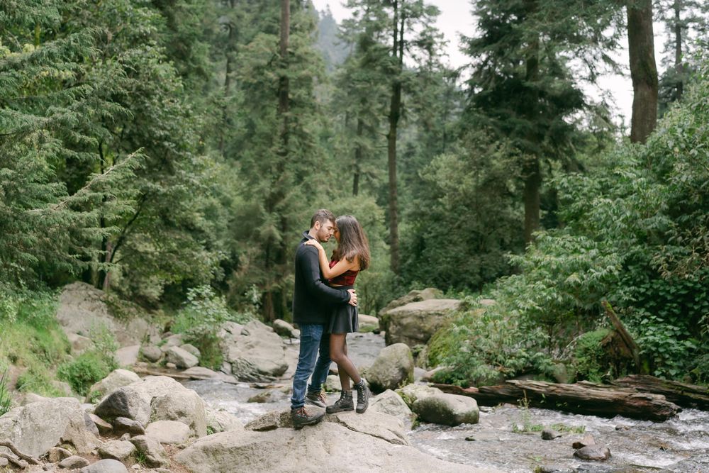 Couple sharing an intimate moment by a stream in a lush evergreen forest.