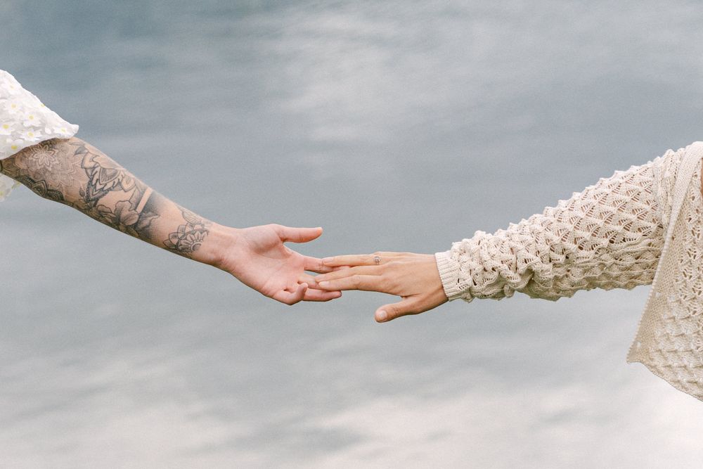 Close-up of two hands reaching towards each other against cloudy background.