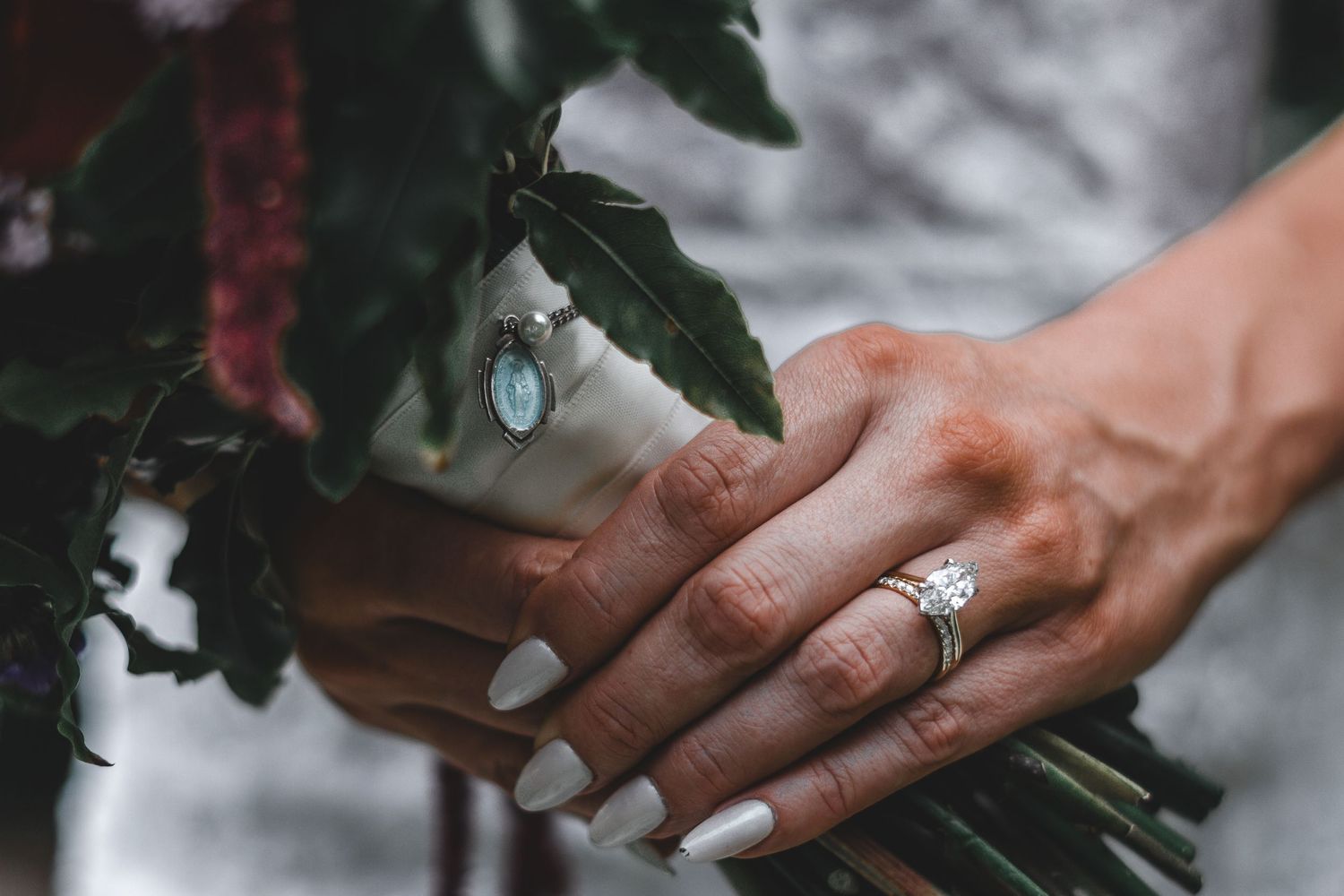 Bride holding bouquet, details on wedding bouquet with a catholic pendant.