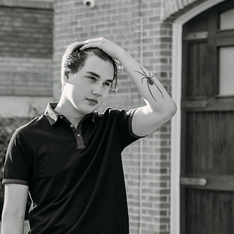 Young guy running his fingers in his hair showing off his spider tattoo.
