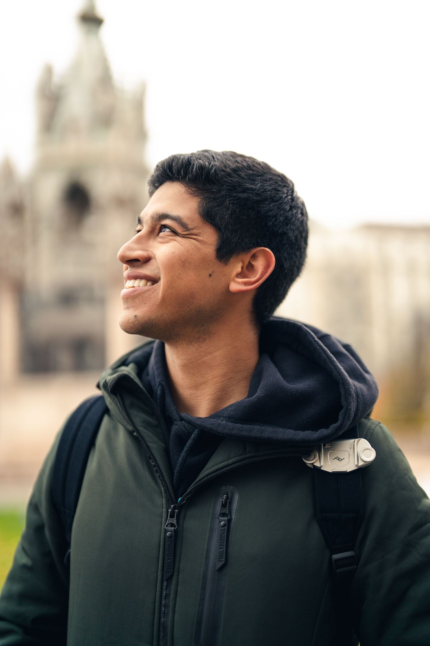 Person in dark hoodie smiling against historic architecture background.