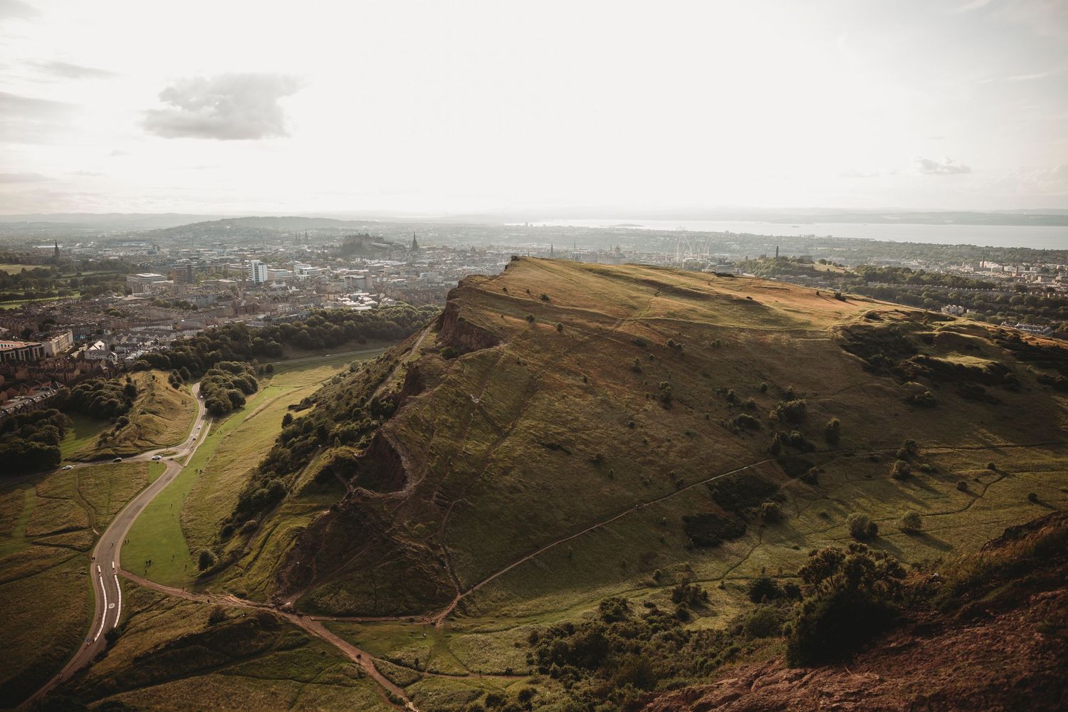 Dramatic aerial view of Edinburgh's Arthur's Seat with winding paths and city vista below.