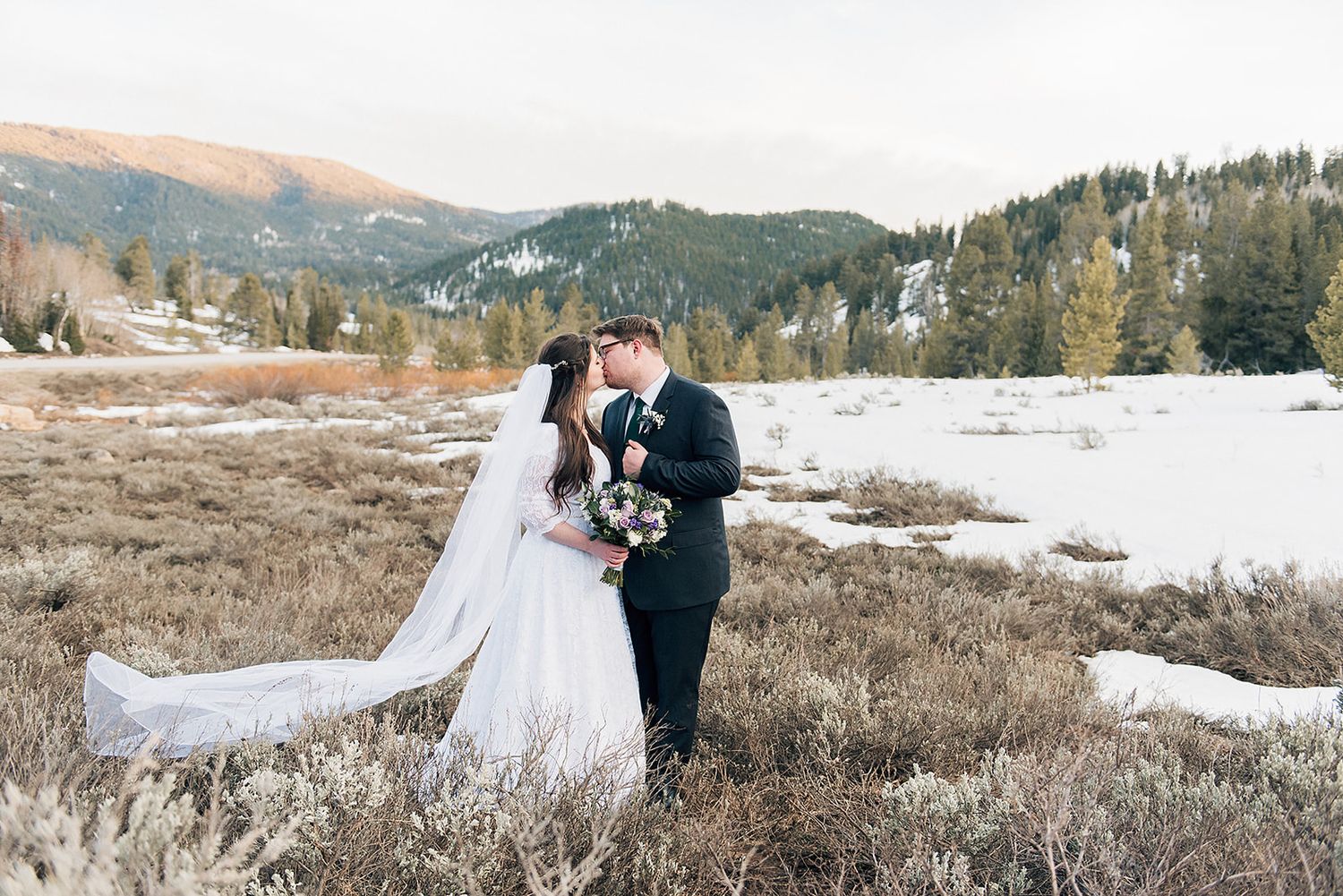 Newlyweds embrace in a snowy mountain meadow during their winter wedding.